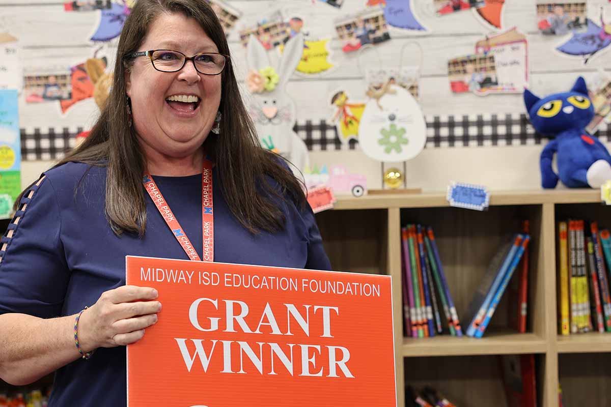 Happy teacher holding a grant winner sign.