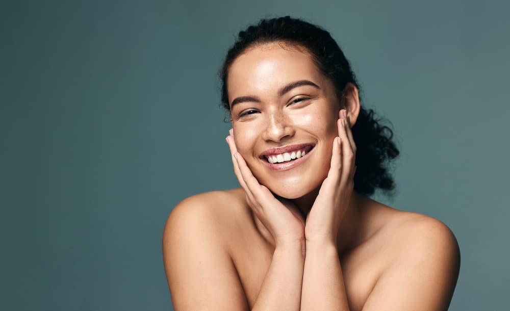 Smiling woman with healthy, glowing skin holding her face, promoting skin care products or cosmetic dermatology services.