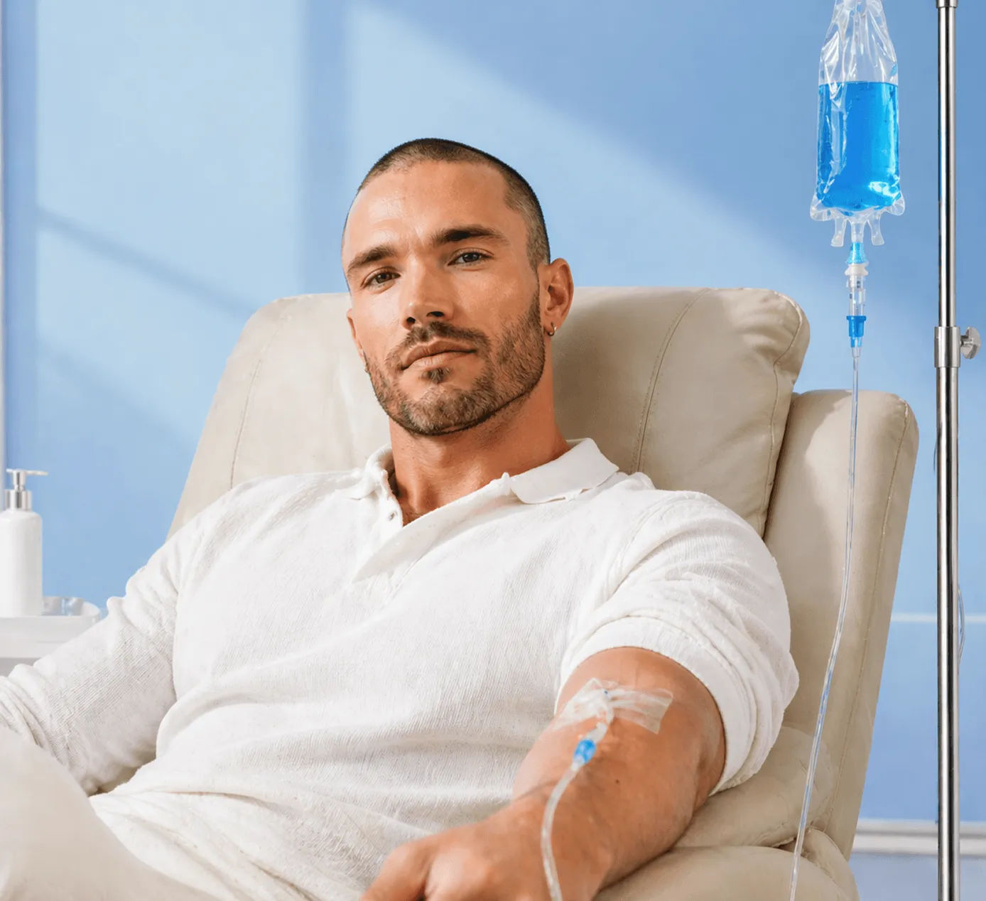 Man in white shirt receiving IV therapy sitting in a beige chair against a blue wall.