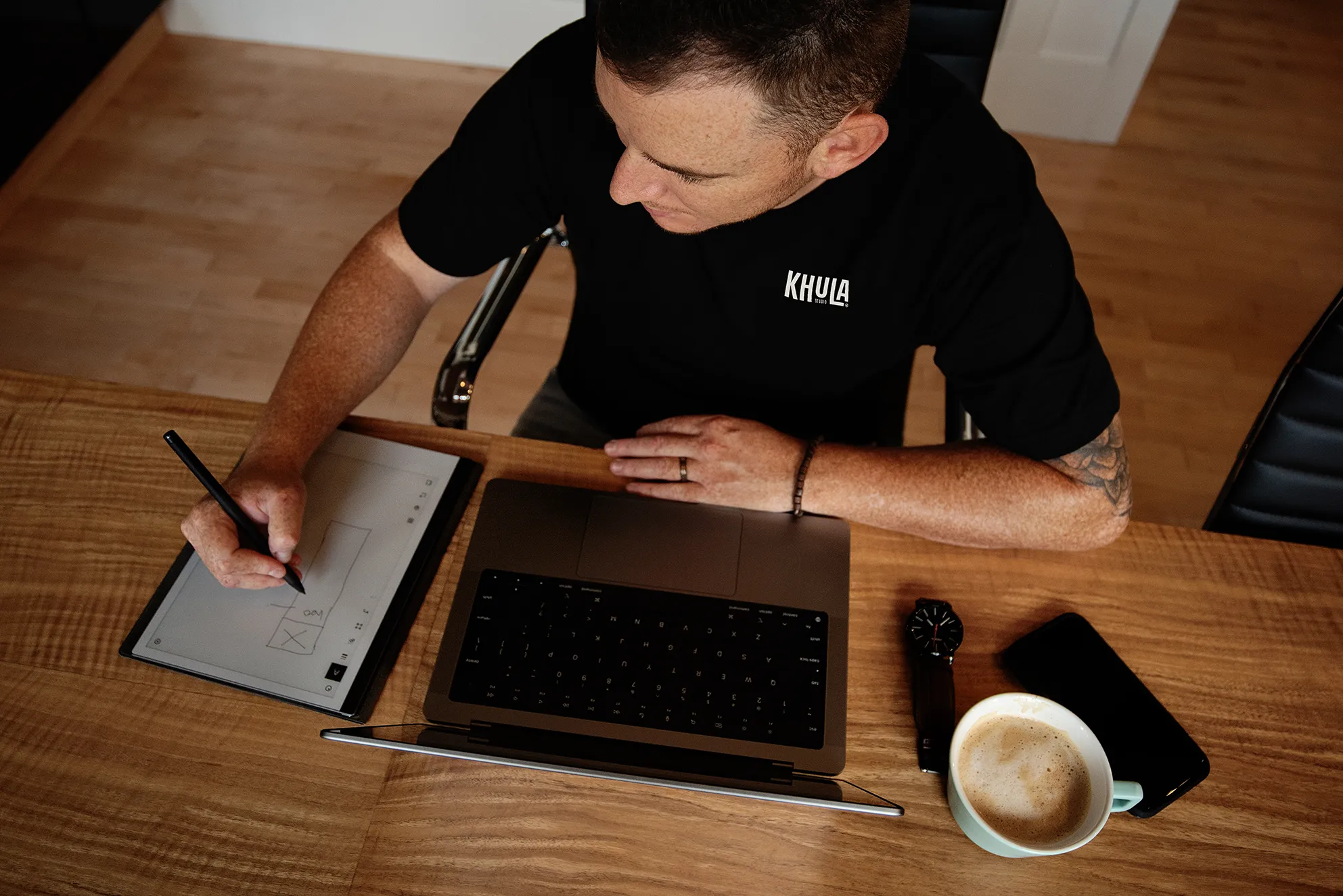 Jamie sits at a table, laptop in hand, diligently writing on a piece of paper.