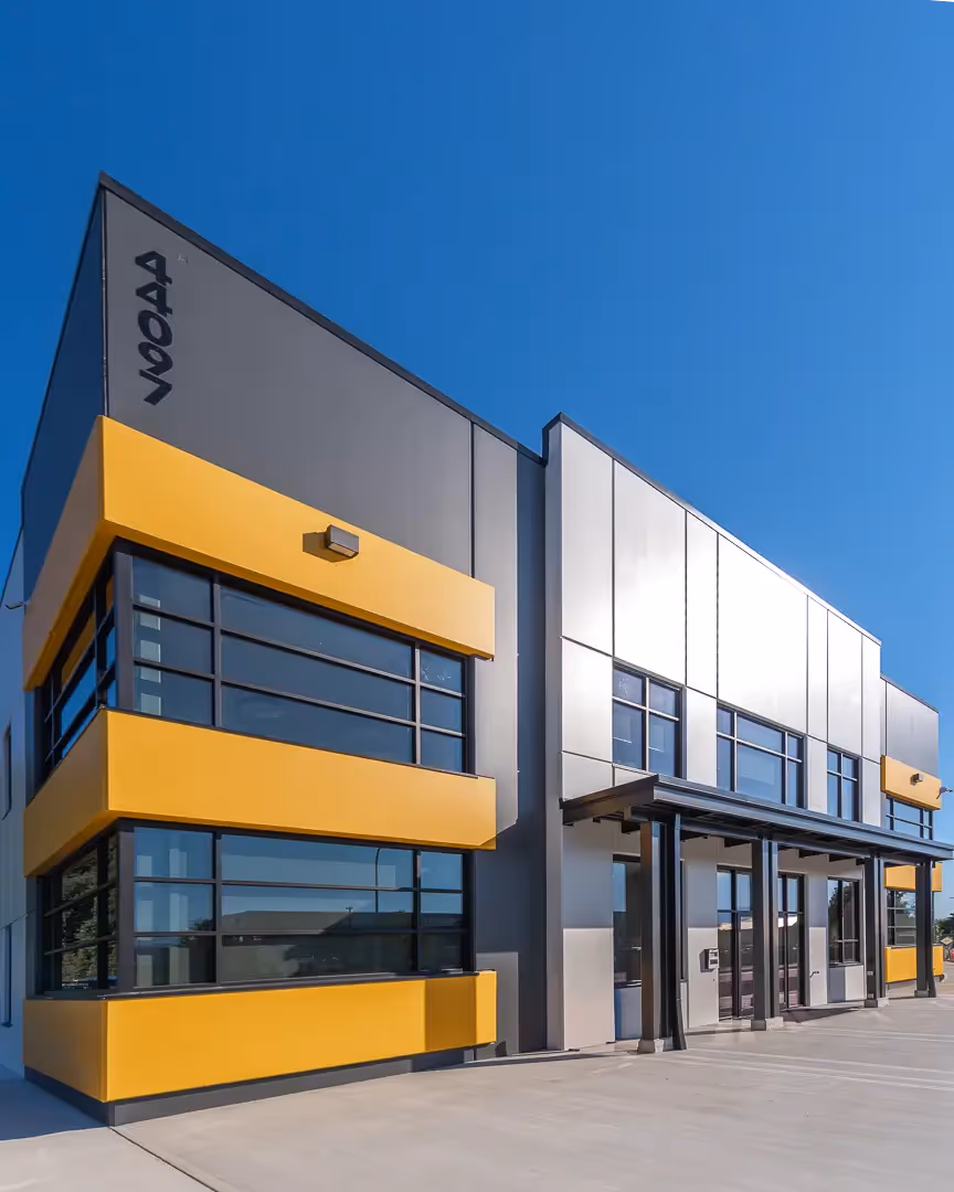Modern commercial building with gray and yellow exterior panels under a clear blue sky.