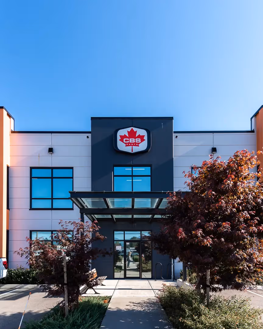 Modern commercial building with black and white facade, large glass windows, and a CBS Parts logo featuring a red maple leaf above the entrance.