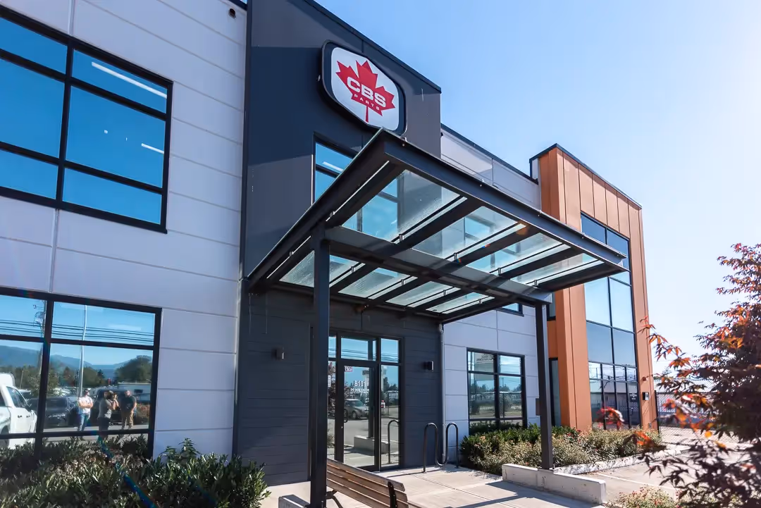 Modern commercial building entrance with glass canopy and CBS Parts logo on the facade.