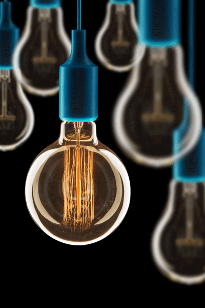 Close-up of a lit vintage-style Edison bulb hanging with a blue socket and blurred similar bulbs in the background against a black backdrop.