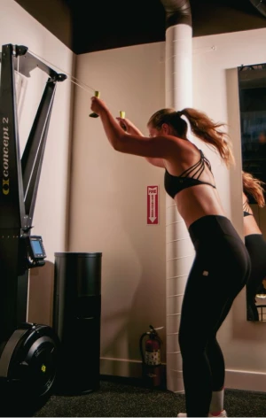 Woman in black workout clothes using a Concept2 rowing machine in a gym.