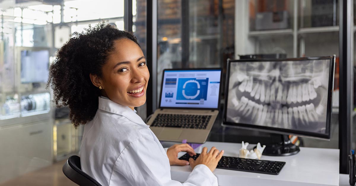 dental care professional works at computer desk with tooth x-ray on-screen