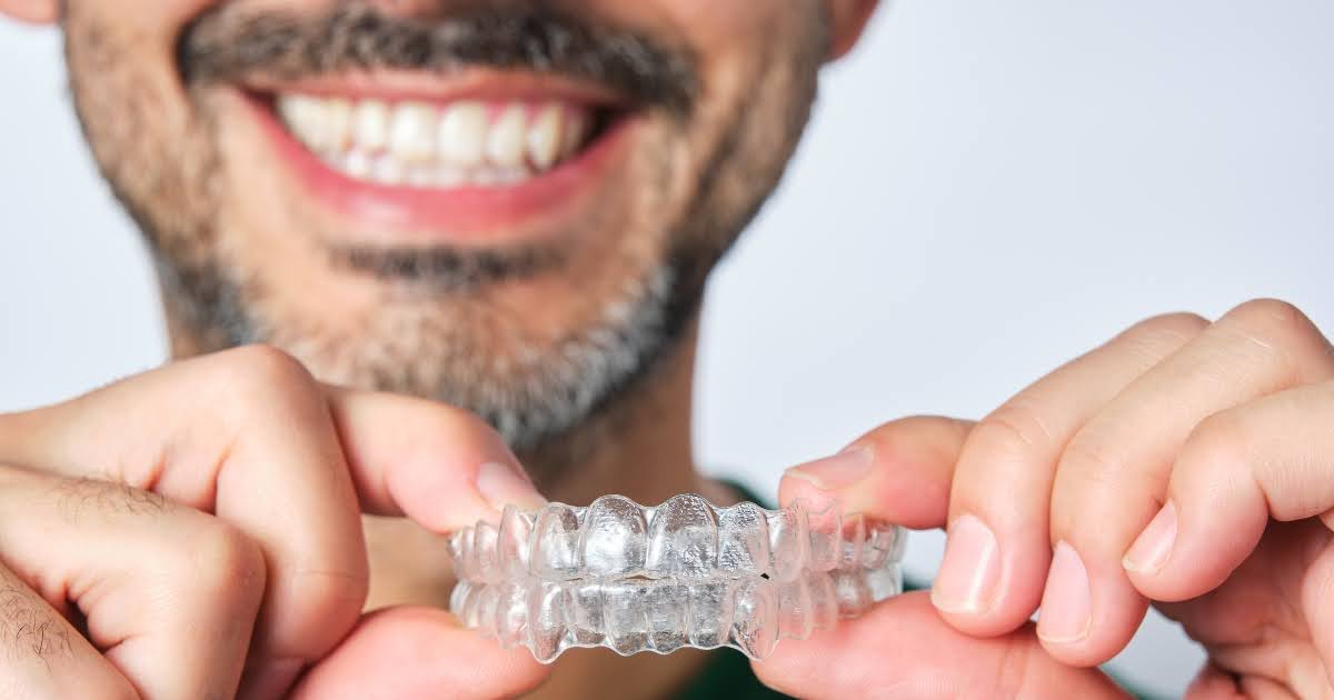 A smiling patient holds clear aligners, representing family dentistry provided by a family dentist near me at a dental office in Mercer Island, WA.