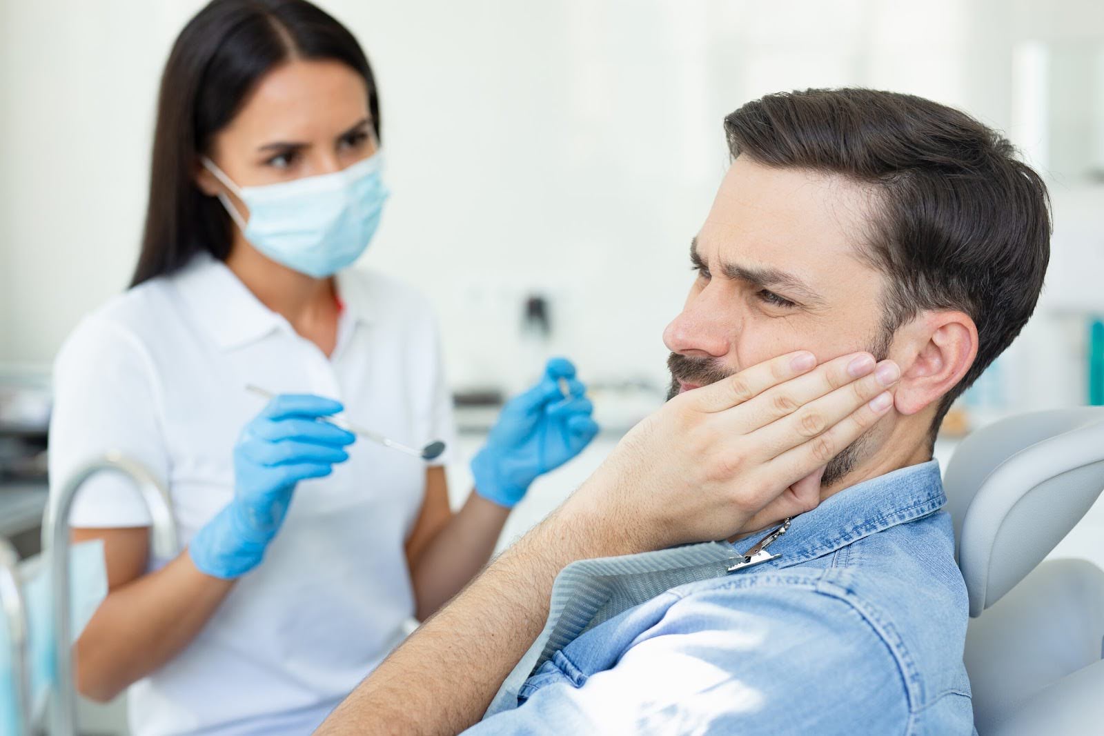 Patient experiencing jaw pain while dentist prepares for examination.