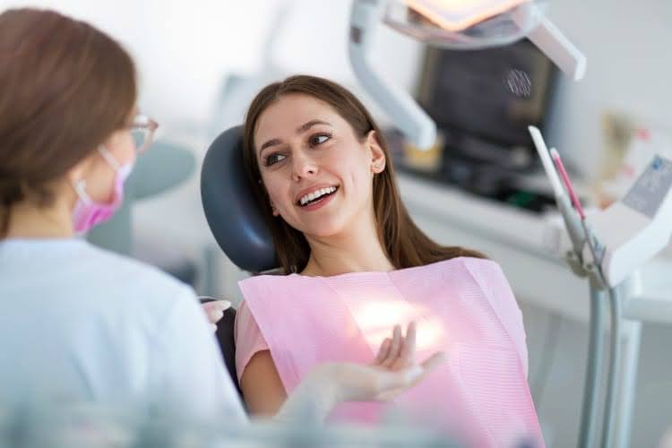 A patient smiling during a dental cleaning while a dental hygienist discusses with her.
