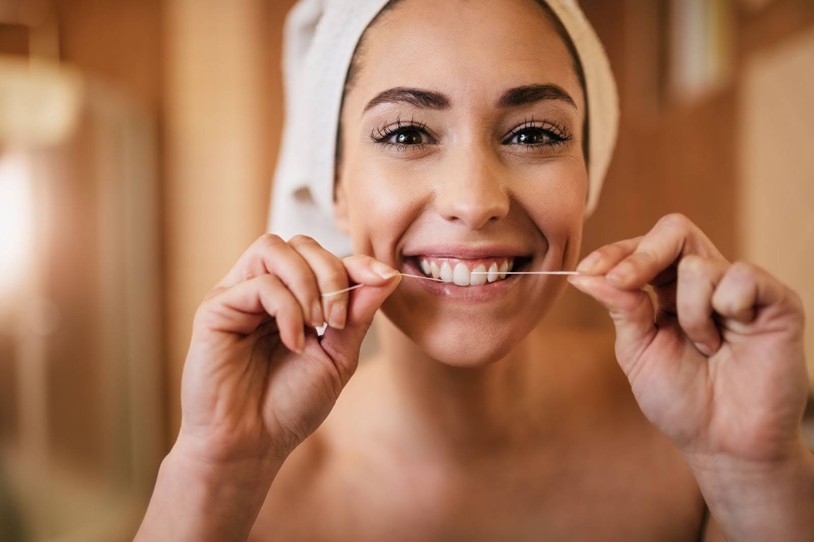 A dental hygienist performing a checkup on a patient who is holding a mirror to inspect her teeth during a dental cleaning.
