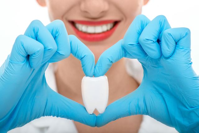 Smiling woman holding a tooth-shaped model in a heart shape, symbolizing dental care and wisdom teeth removal.