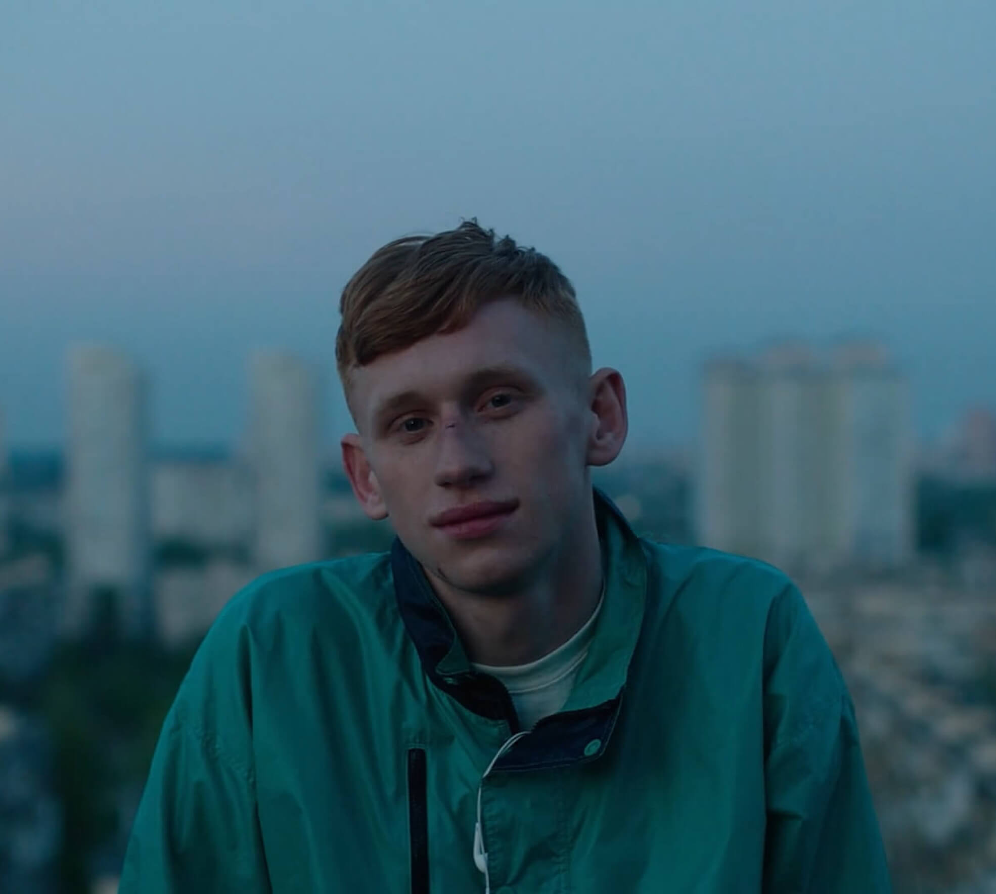 The male protagonist from short film goodbye golovin smiling into the camera with a city backdrop in the distance