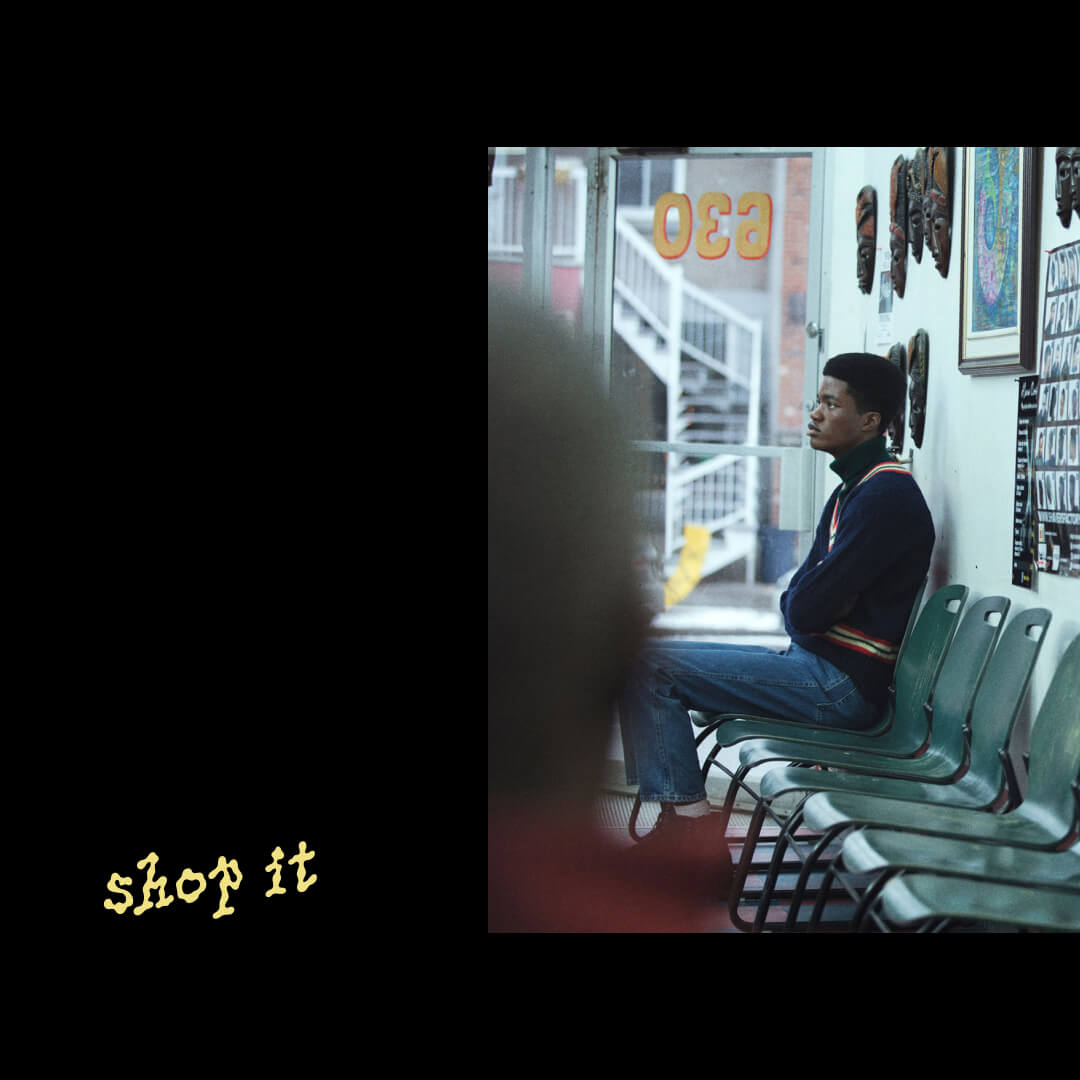 A photo of black man sits alone on a row of teal chairs at a barbershop. There are yellow words written in a funky font that read "shop it" next to this photo on a black background.