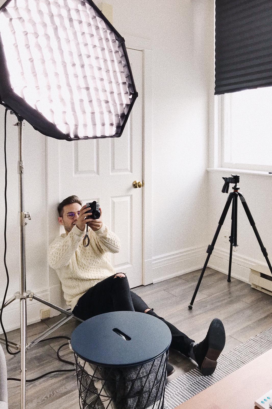 Photo of Alex Presa sitting on the floor with back to the wall, holding up a film camera