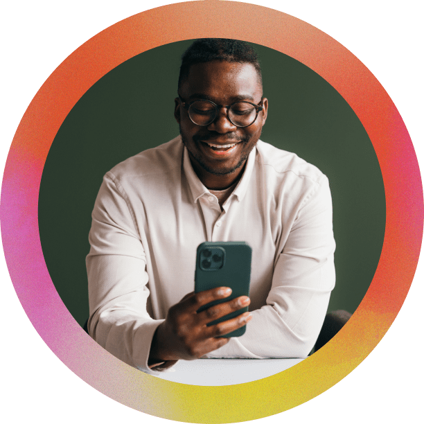 A smiling man with glasses and a light shirt looks down at a smartphone he is holding. The portrait is framed by a thick circular border with an orange, pink, and yellow gradient.