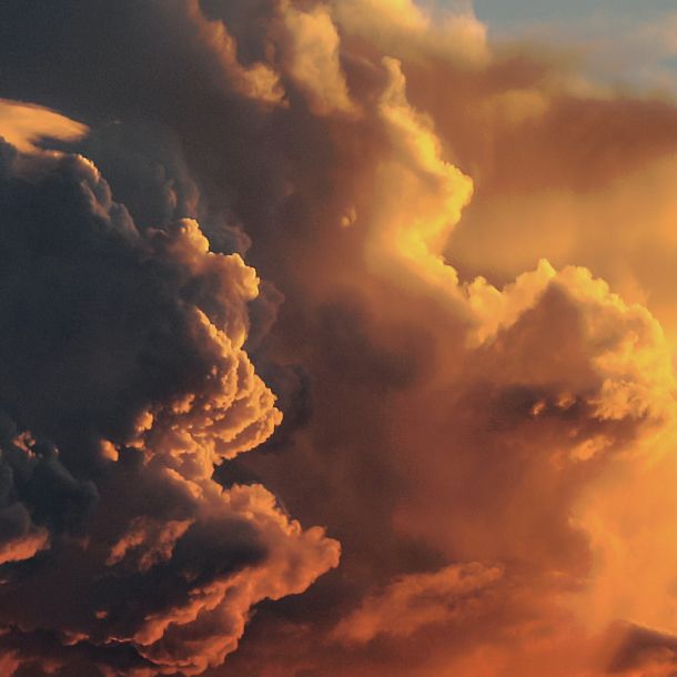 Towering storm clouds glow orange and gold in warm sunlight, with darker gray clouds filling the left side.