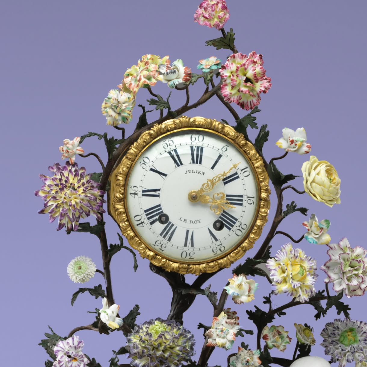 An ornate golden astronomical instrument features multiple concentric dials, Roman numerals, and fine engraved markings against a lavender background.