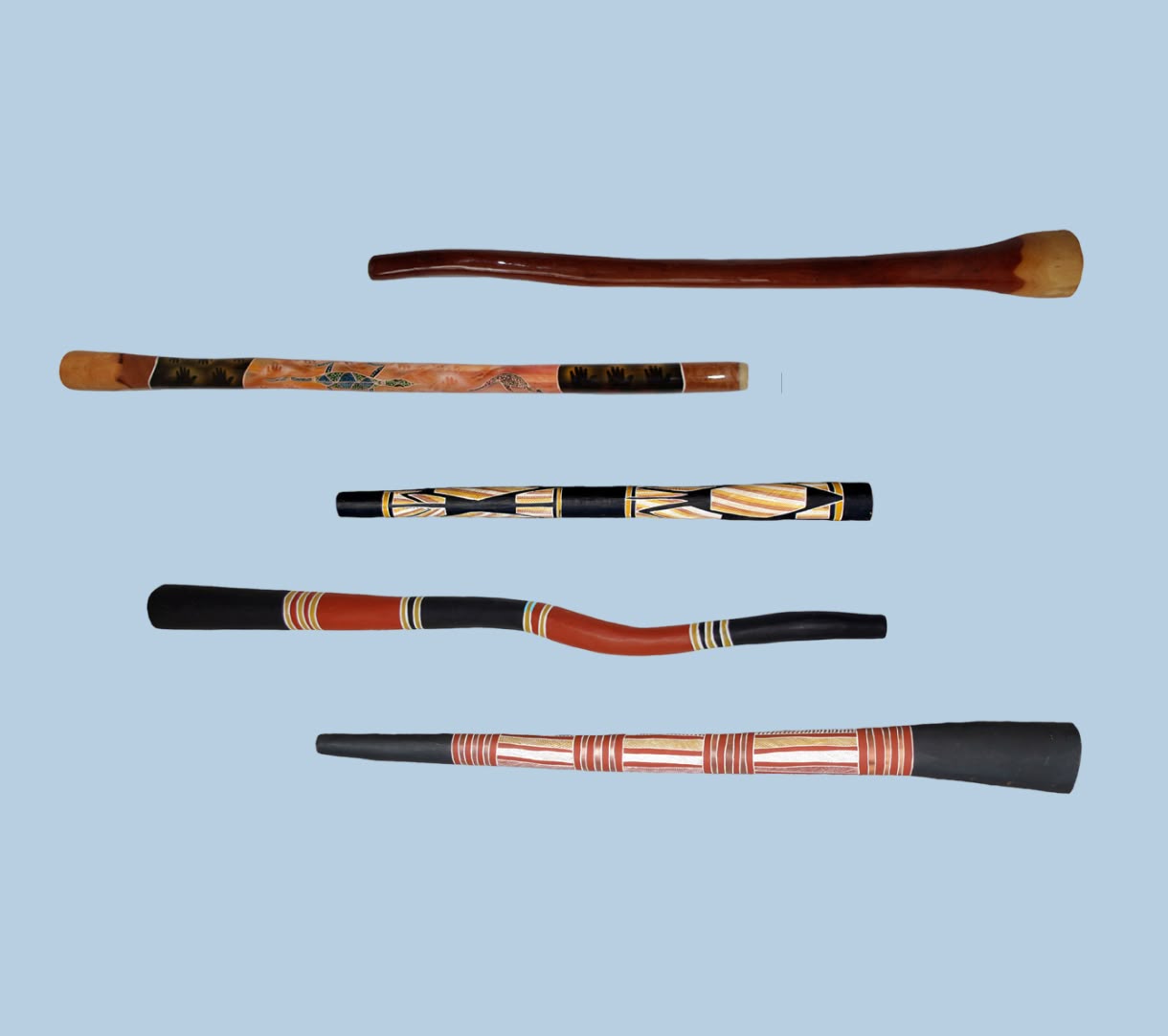Five decorated didgeridoos in red, black, ochre, and brown stand upright against a pale blue background.