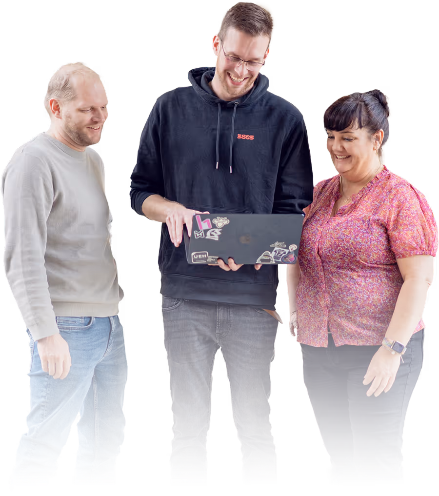 Drei lächelnde Menschen stehen zusammen, wobei die Person in der Mitte einen Laptop mit Aufklebern zeigt.