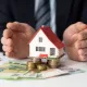 Cette image montre une personne tenant une maquette de maison et de l'argent entre ses mains