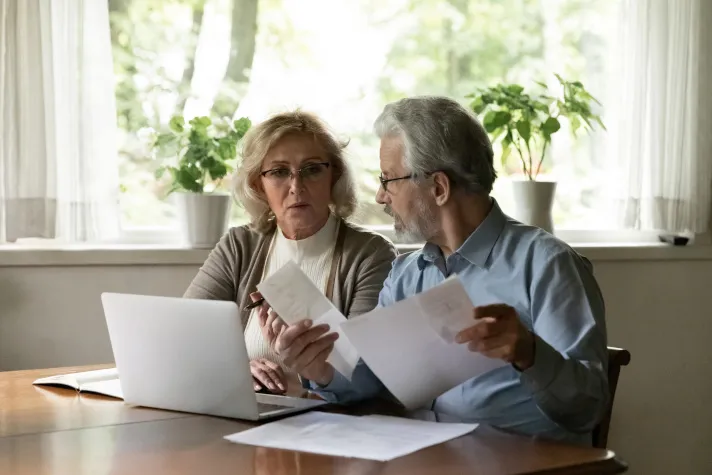 Cette image montre un couple de personnes seniors examinant des factures 