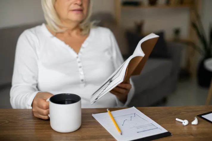 Cette image montre une femme lisant un livre en prenant des notes