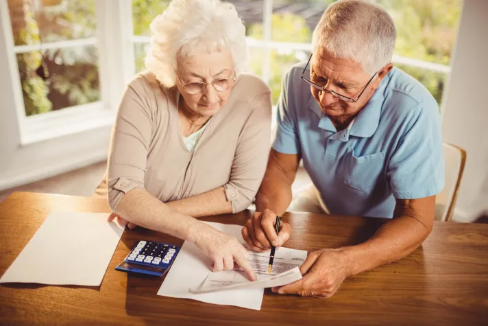Cette image montre un couple de senior vérifiant des documents comptable avec une calculatrice
