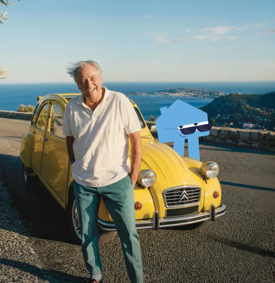 Cette image montre un homme senior souriant, devant une voiture ancienne, accompagné de la mascotte d'Arrago