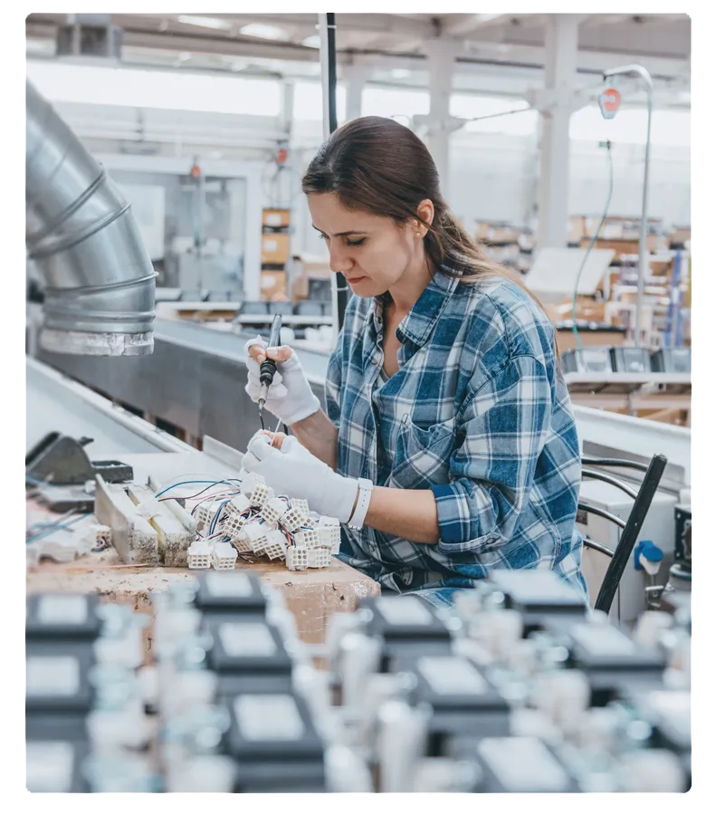 Woman soldering electrical connectors at a workstation in a manufacturing facility.