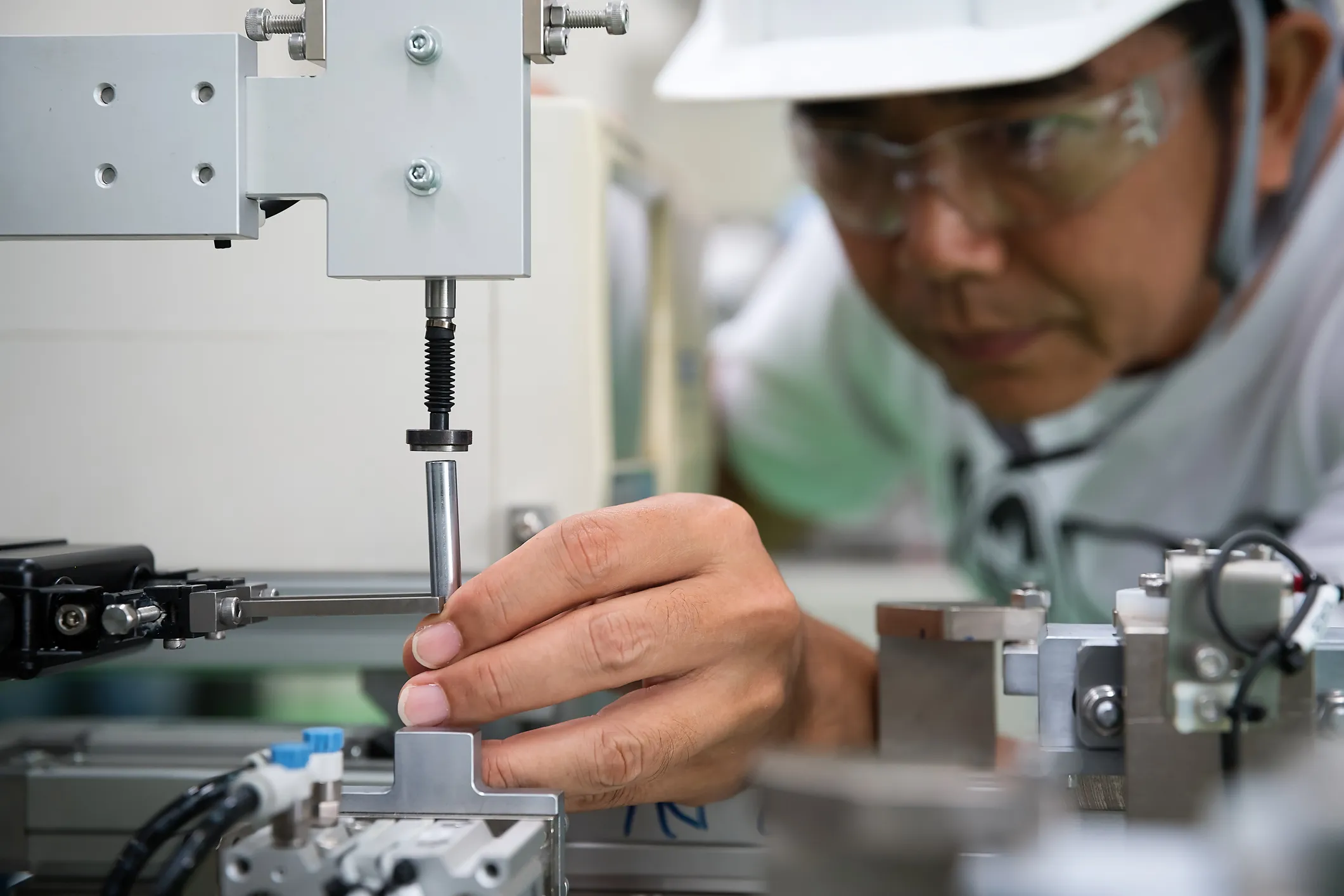 Technician wearing safety glasses adjusting a metal component on industrial machinery.