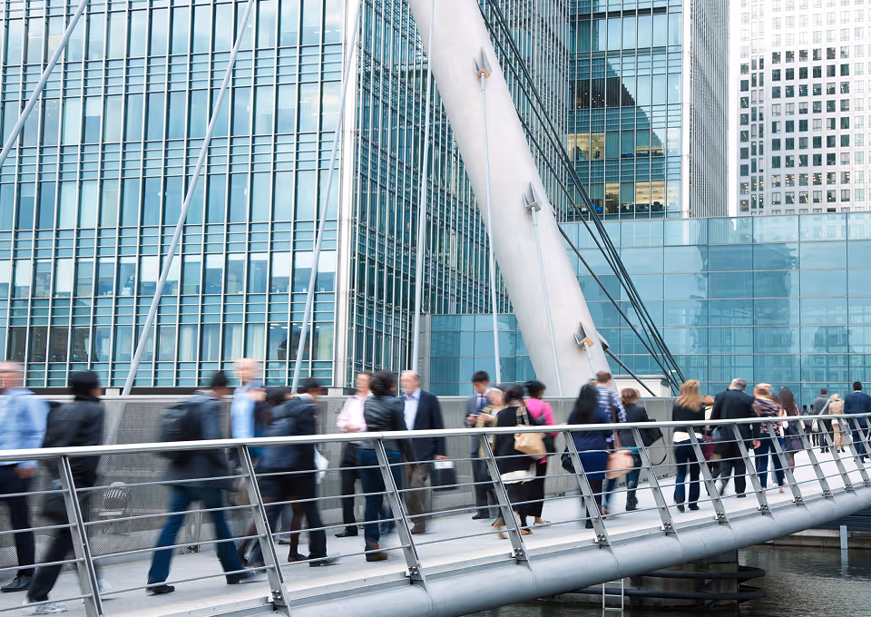 Commuters walking across a bridge outside glass office buildings.