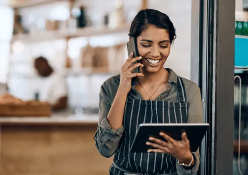 Hospitality worker in apron using phone and tablet in café