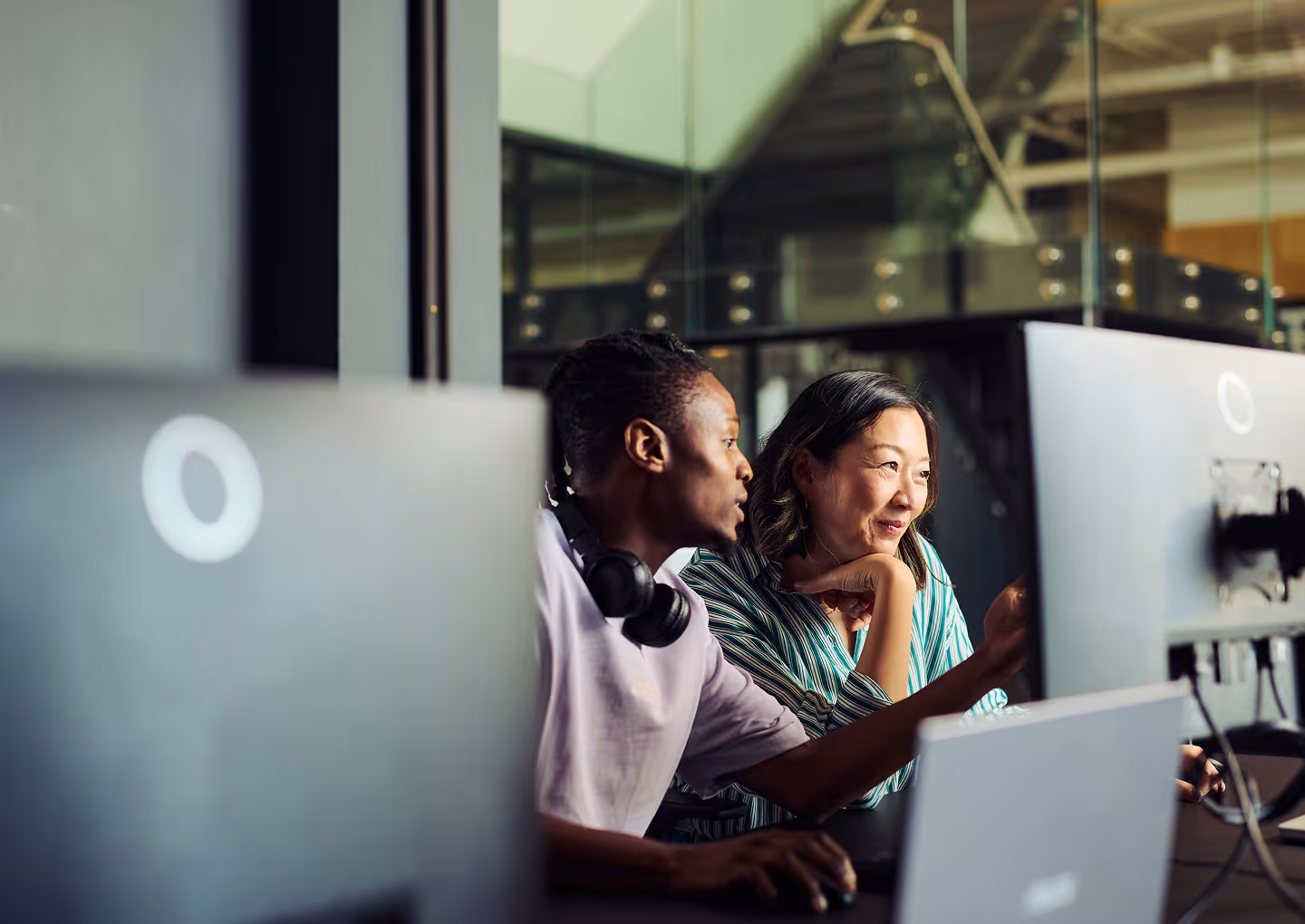 Two colleagues collaborating at desktop monitors in a tech office