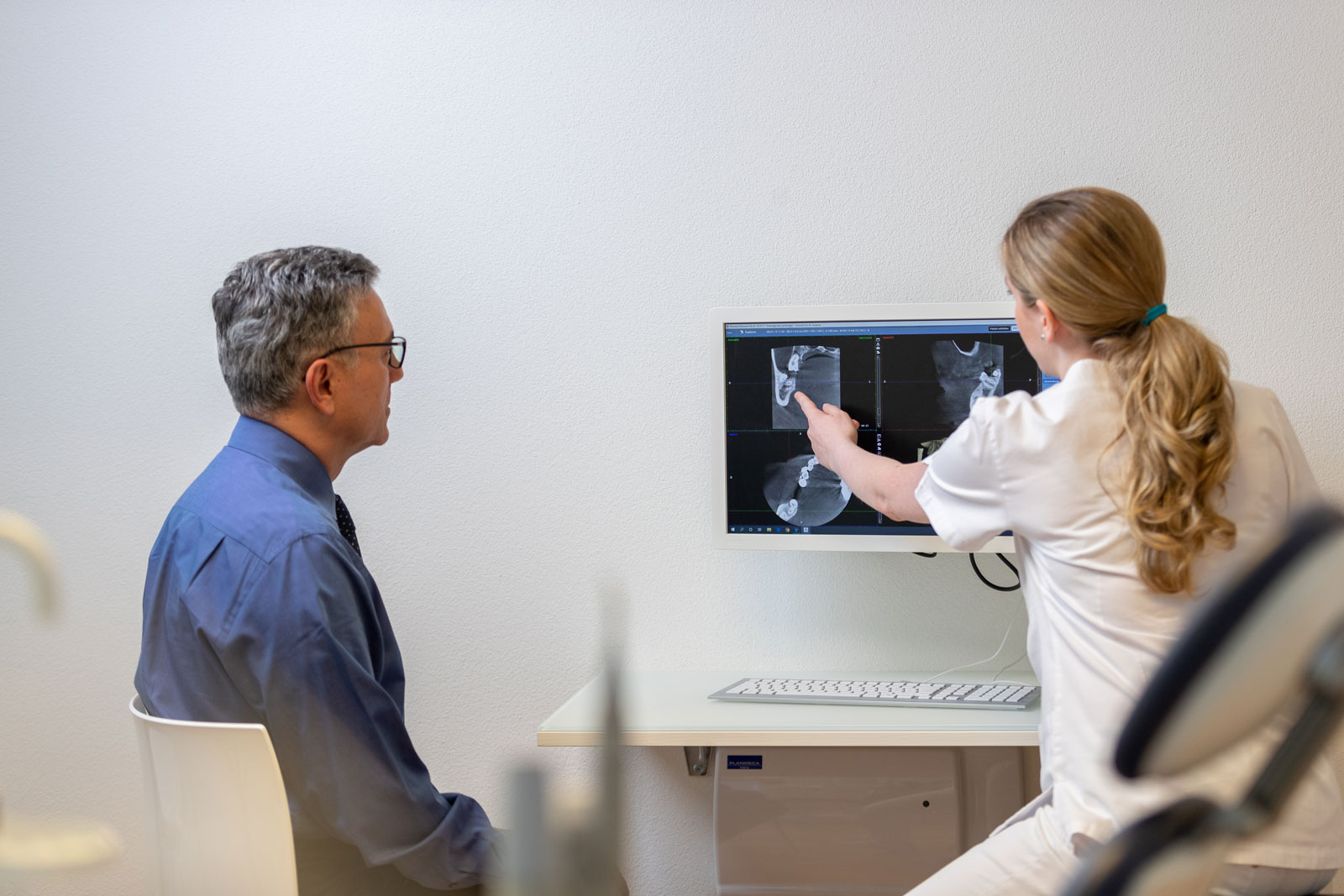 Eine Dentalassistentin berät einen Kunden zur Wurzelbehandlung. Die Wurzelkanalbehandlung erhält den natürlichen Zahn.