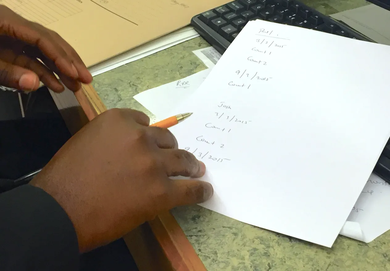 Court staff hold pen in hand just above an a4 piece of paper resting on a desk alongside a keyboard.