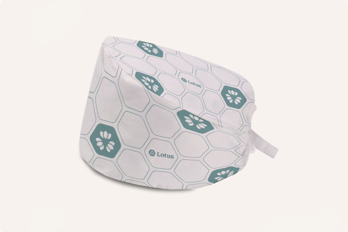 White medical scrub cap with hexagonal pattern and teal floral icons, featuring the word Lotus printed on it.