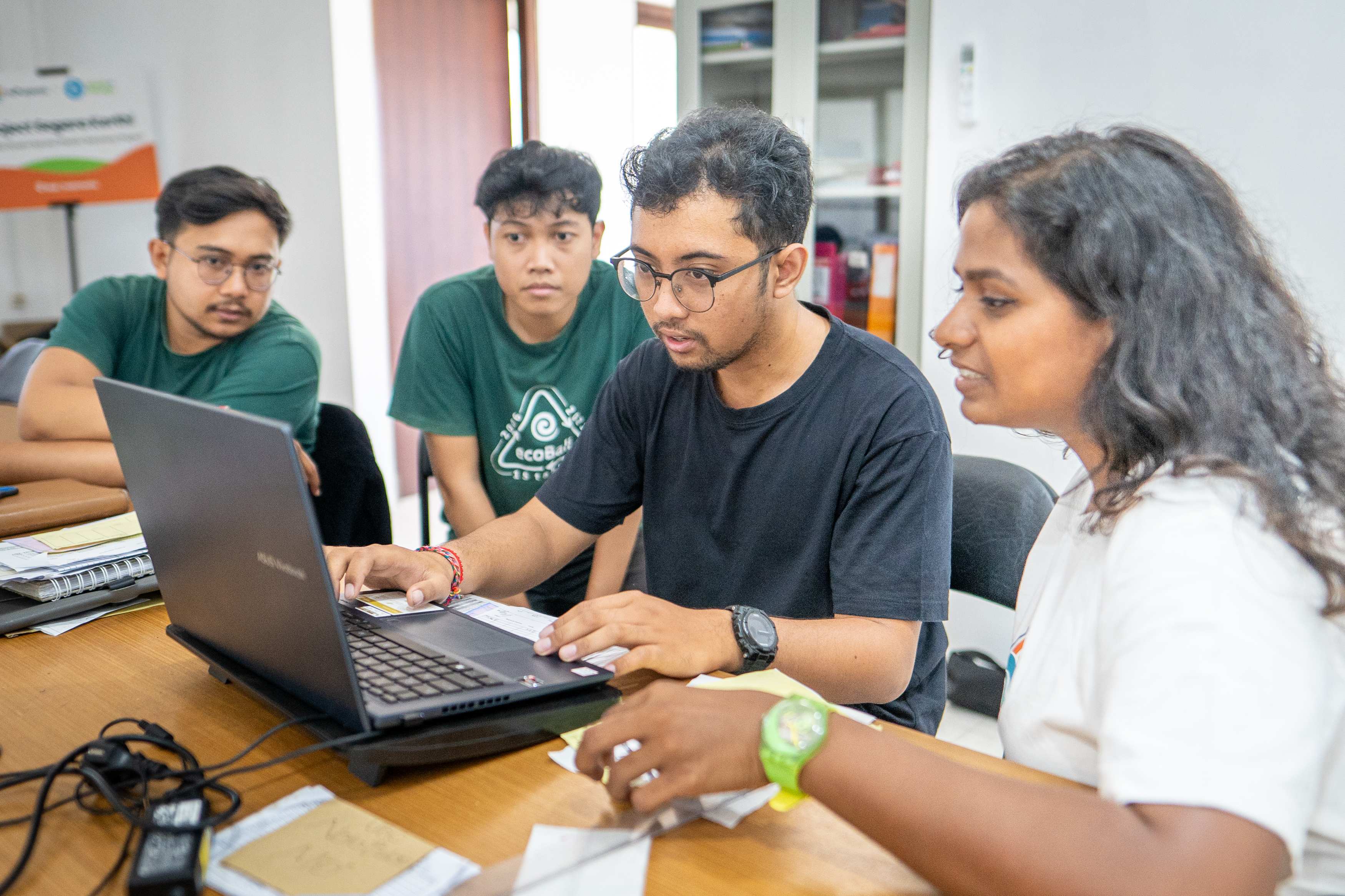a group of people sitting around a table looking at a laptop