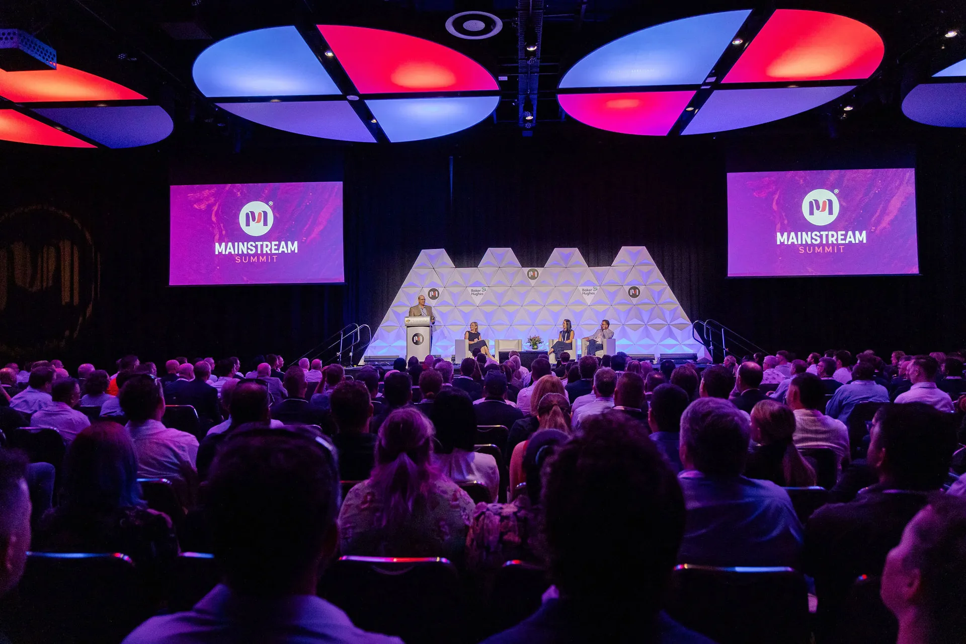 Audience facing a stage with four speakers at the MAINSTREAM Summit