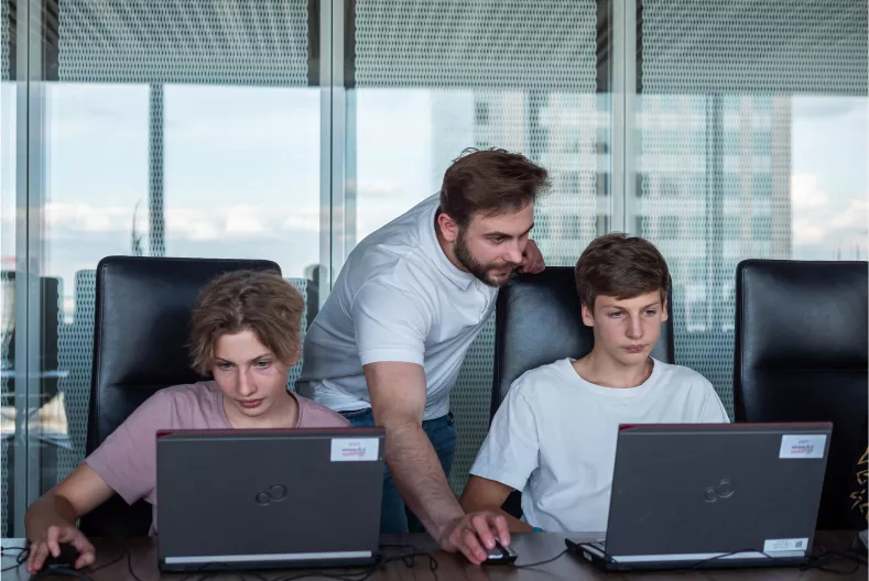 Instructor assisting two students working on laptops.