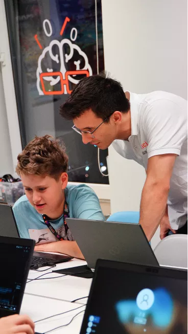 Teacher guiding a student working on a laptop.