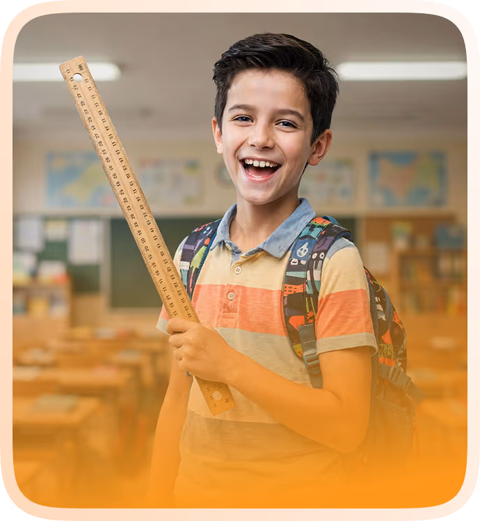 Smiling schoolboy wearing a colorful striped polo shirt and backpack, holding a wooden ruler vertically in a classroom setting with desks and maps on the walls in the background.