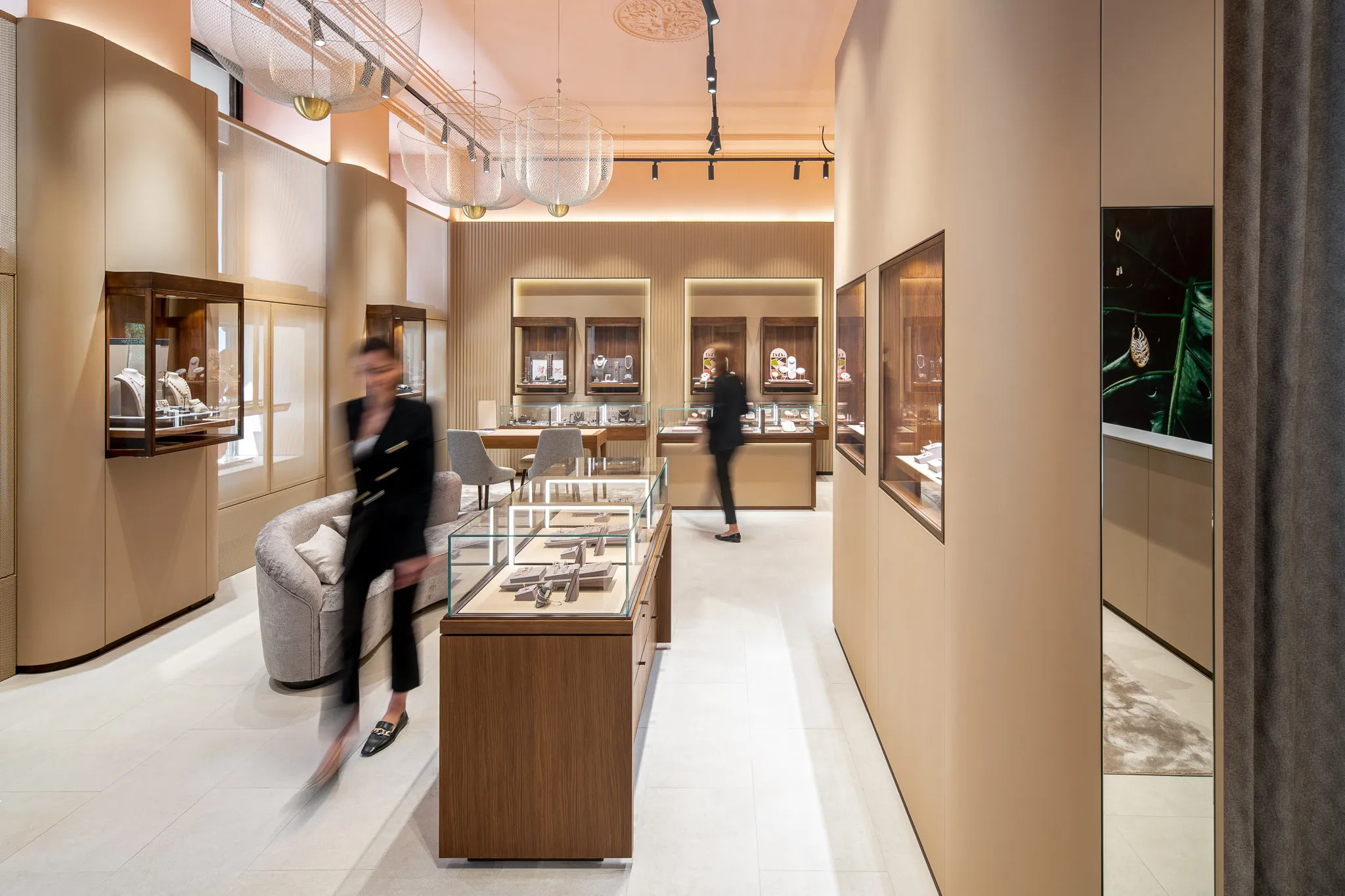 Contemporary jewelry store interior at Malalan Ljubljana, with customers browsing luxury pieces in illuminated glass cases, blending retail movement with premium design by Studio Mosh.