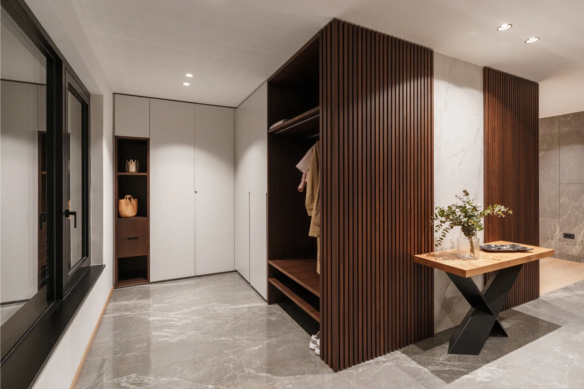 Contemporary entryway with marble flooring, wood slatted wardrobe, and natural wood table with floral decor.