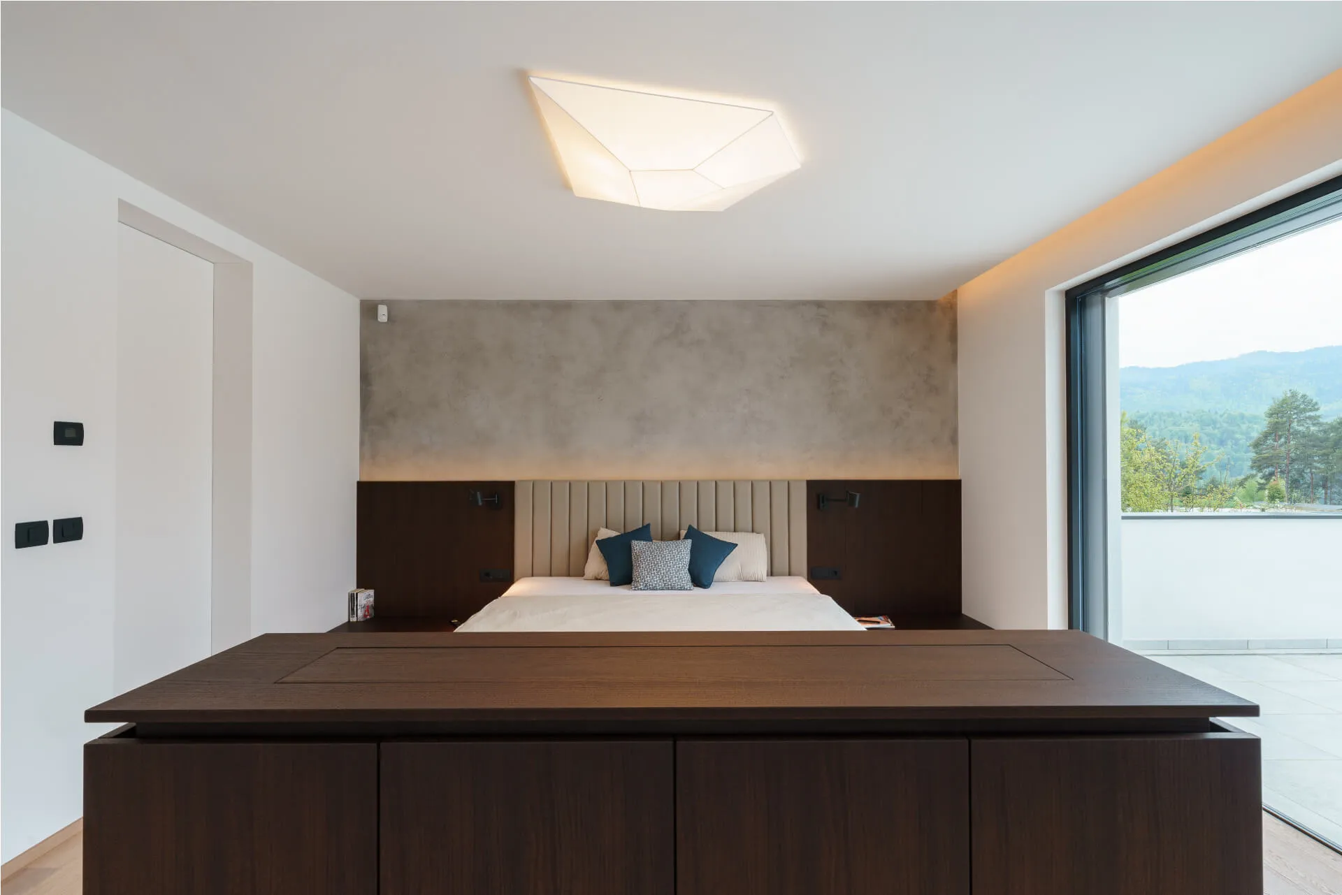 Minimalist bedroom with feature lighting, neutral palette, and panoramic sliding doors overlooking nature.