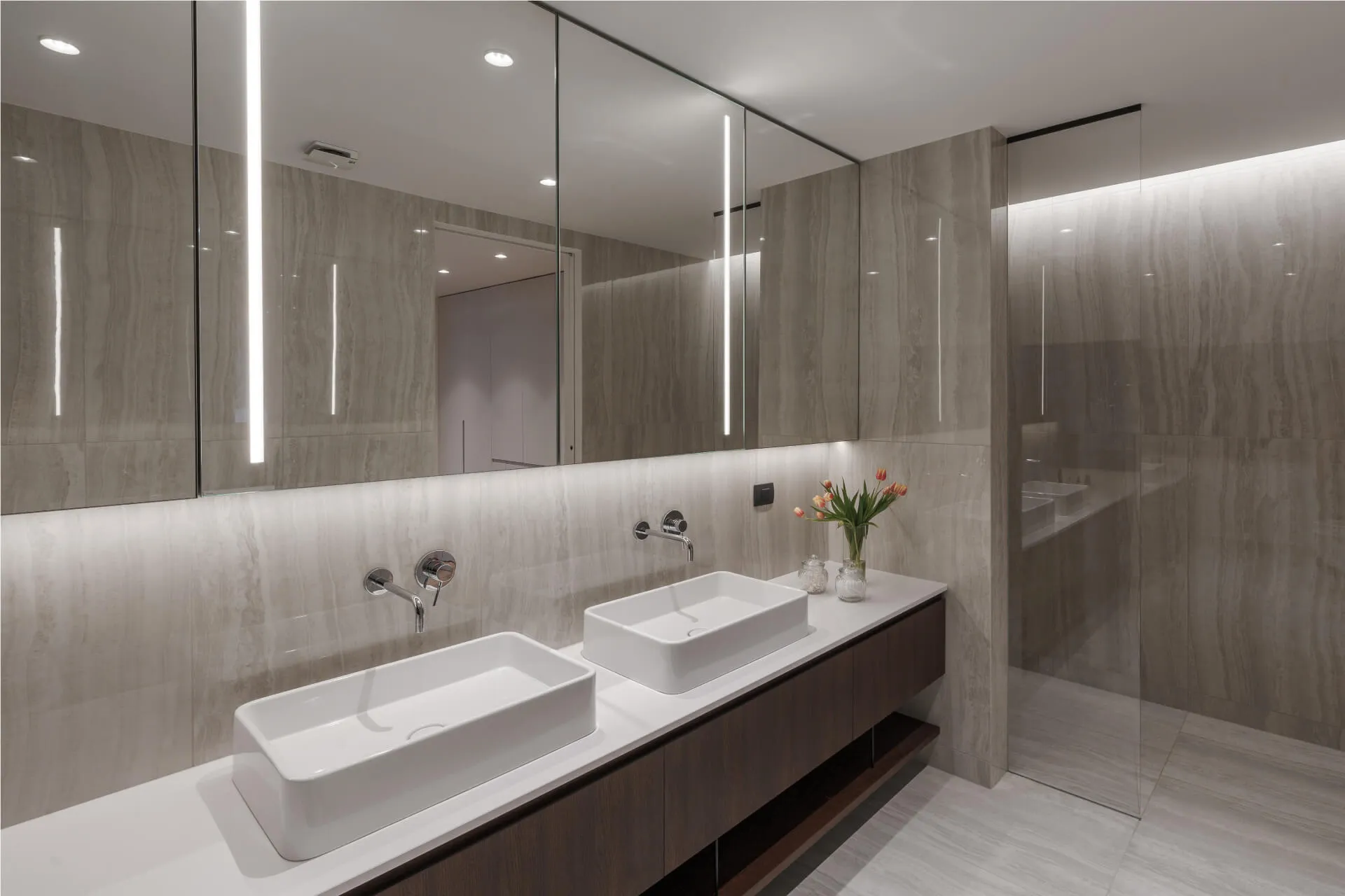 Double sink bathroom vanity with wall-to-wall mirror, modern lighting, and marble wall tiles.