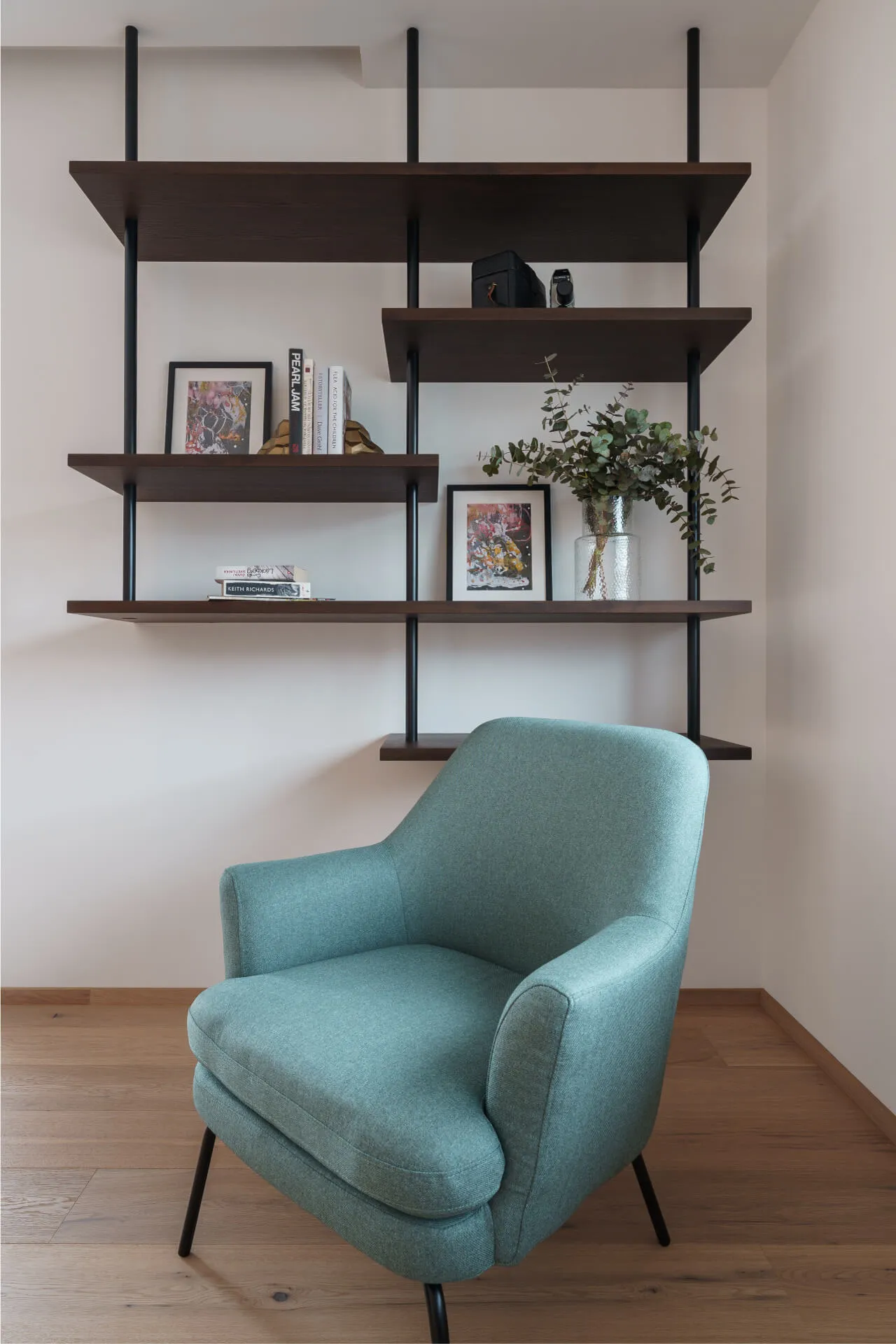 Cozy reading corner with teal armchair and minimalist wall-mounted dark wood shelves.