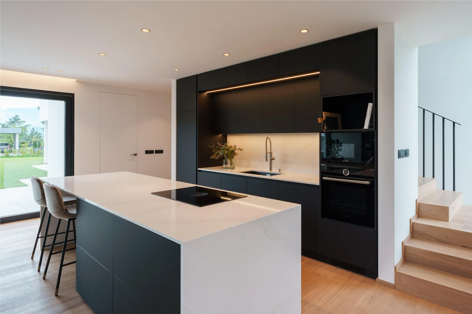 Sleek black and white kitchen design with large island, induction cooktop, and built-in appliances in a modern home.