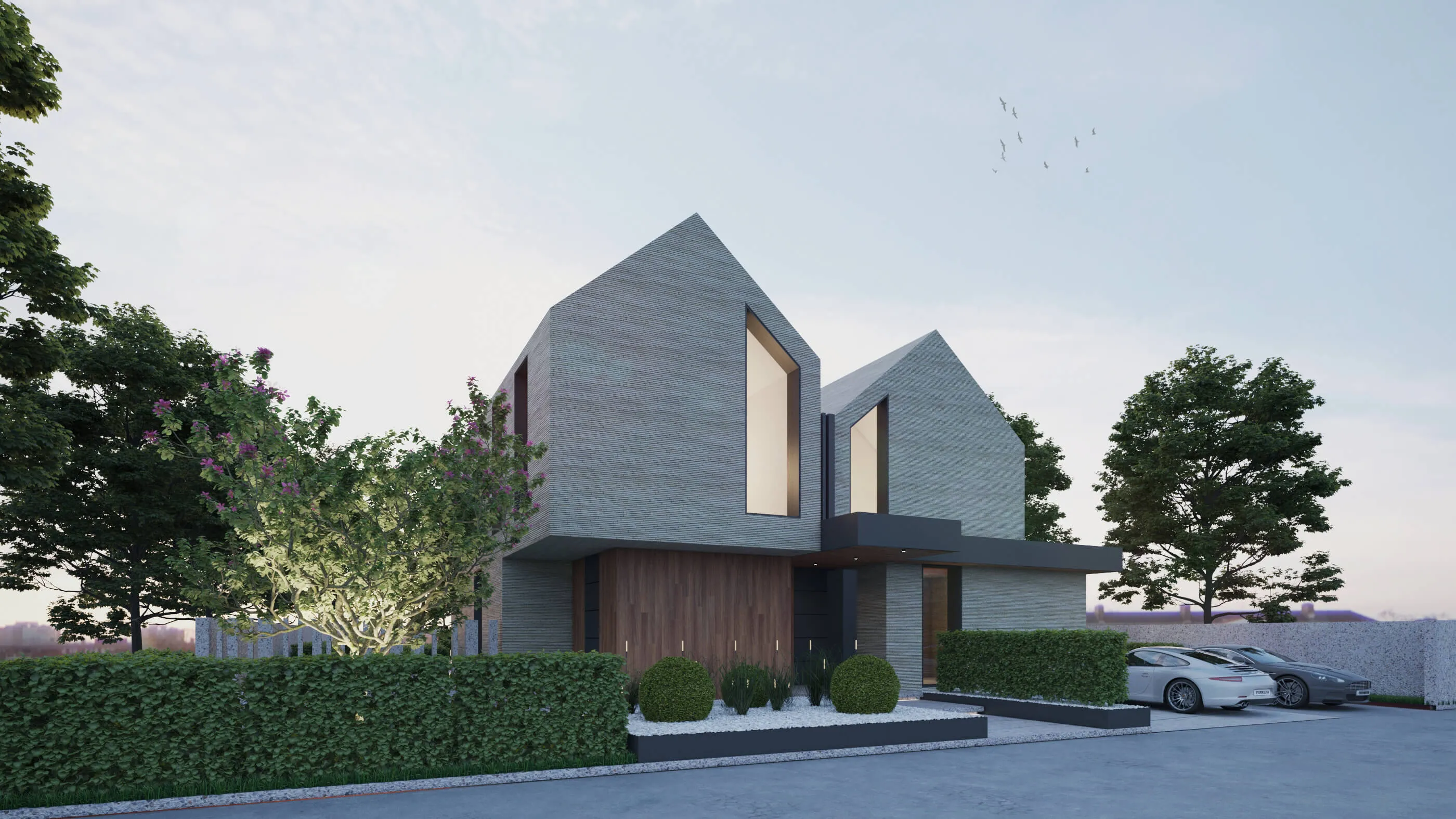 Front view of a contemporary twin-gabled residence with sharp rooflines, geometric architecture, and a clean driveway flanked by sculpted bushes and parked cars.