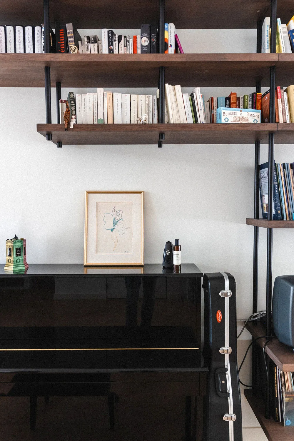 Contemporary piano nook with custom open shelving, decorative objects, and a framed artwork — designed by Studio Mosh for a refined, creative living space with architectural bookshelves.