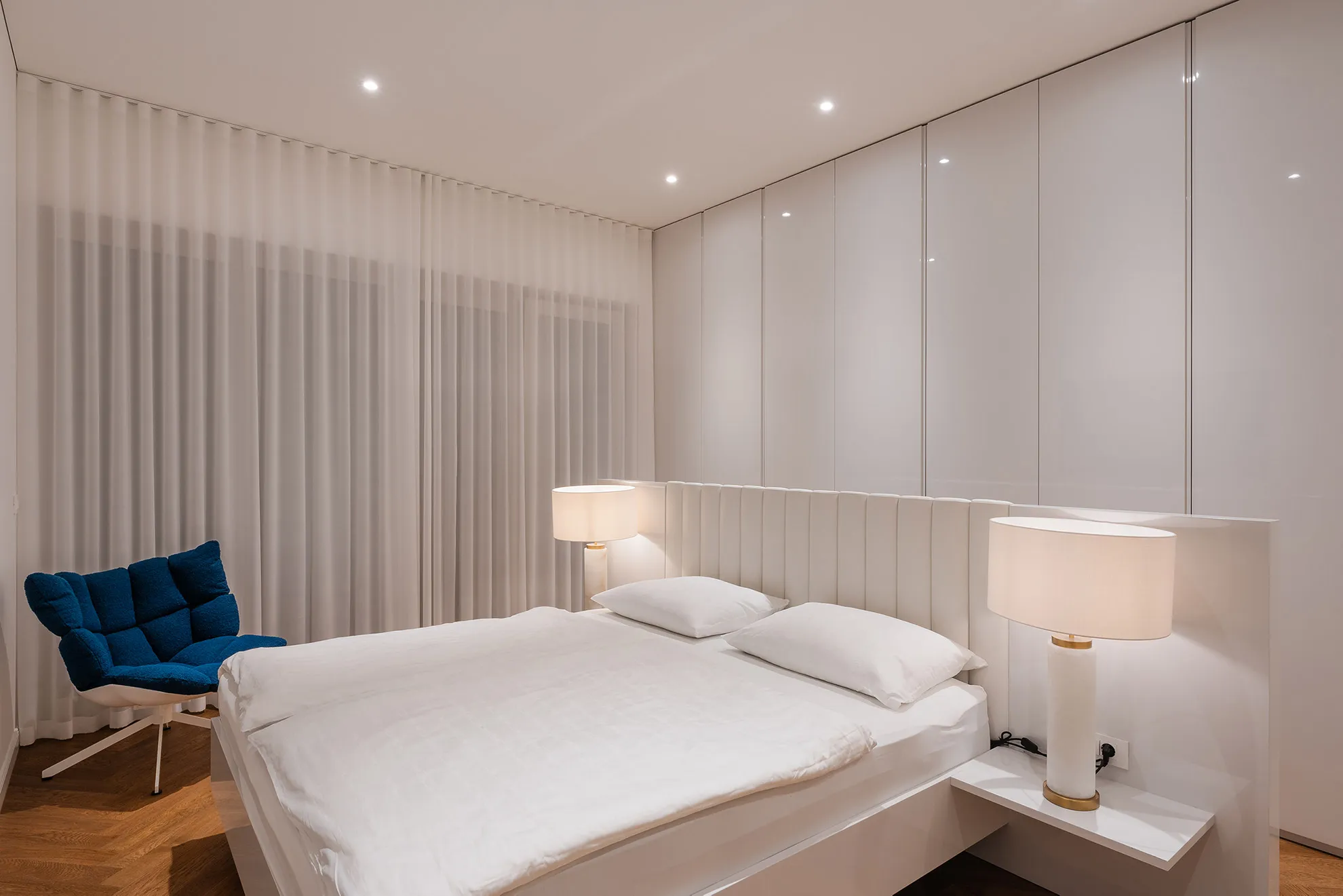 Stylish and minimalist master bedroom in the Penthouse Schellenburg with glossy surfaces, ambient lighting, and modern built-in closets, offering a serene atmosphere in Ljubljana.